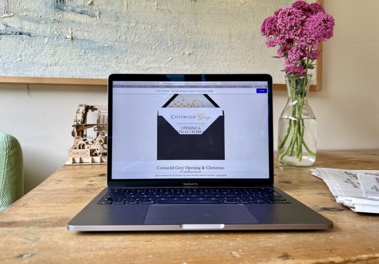 Laptop on wooden table with Cotswold Grey invitation on screen